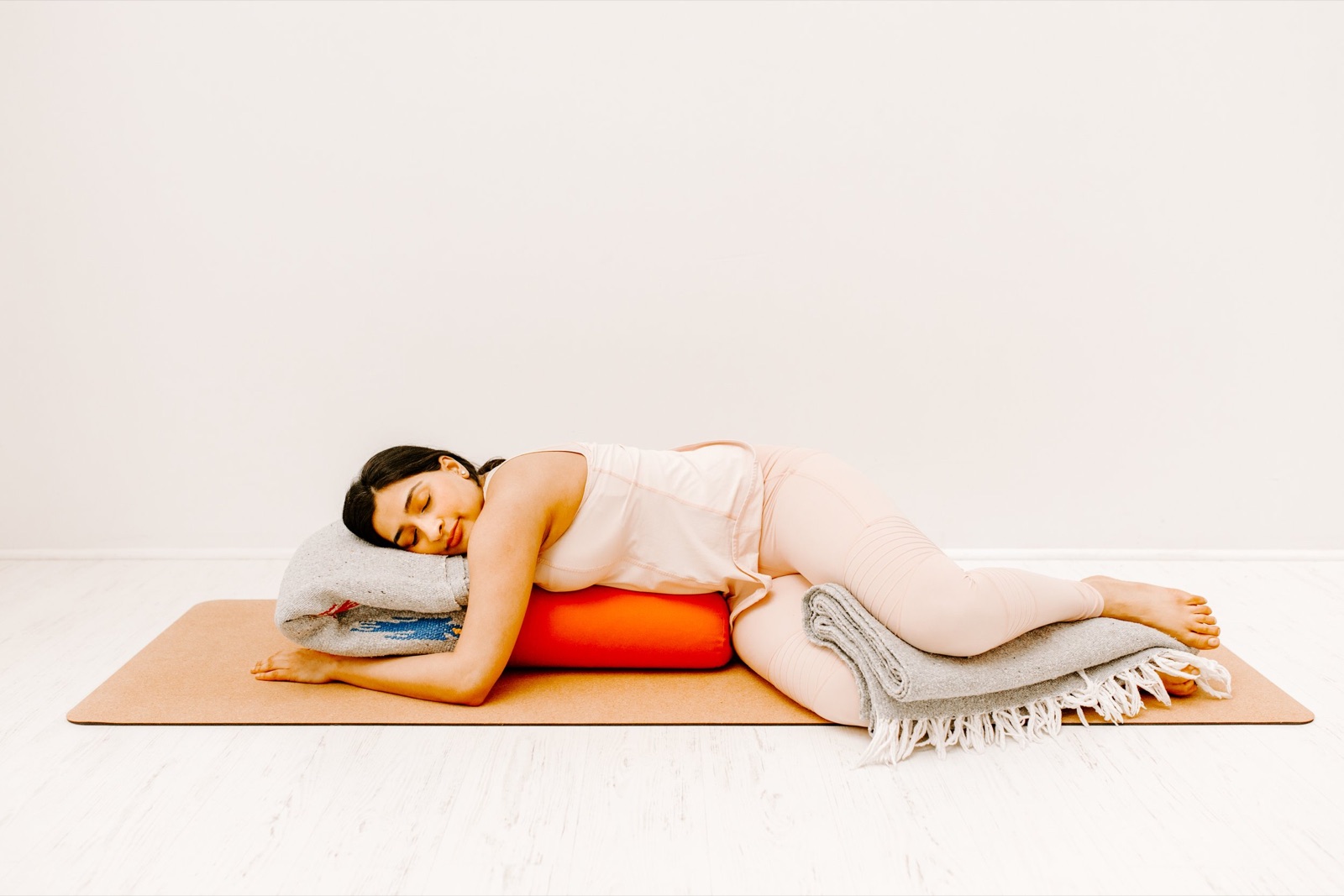 A student lying on her side over a bolster with a folded blanket under her head, fully at rest on the mat.
